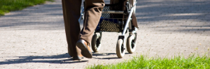 Eine Person geht mit einem Rollator auf einem Weg